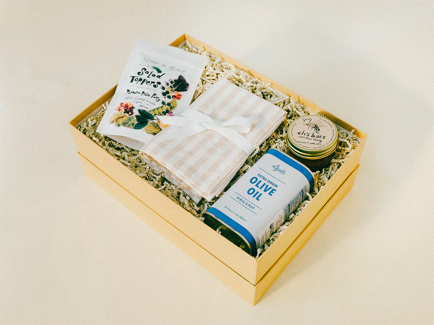 Gift box with pantry items including honey, olive oil, and a striped tea towel.