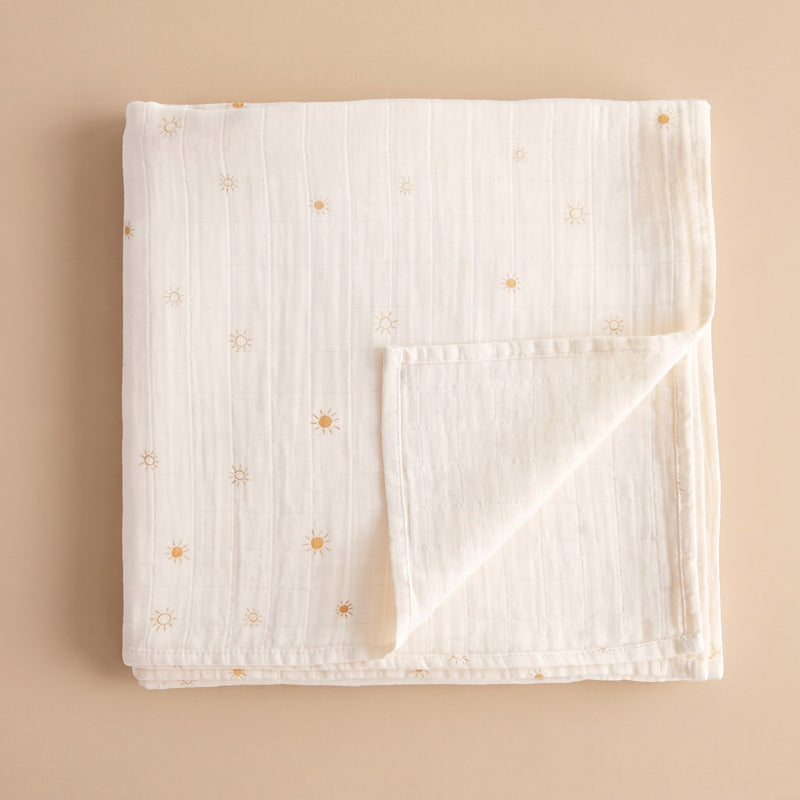 Folded cream organic cotton muslin swaddle with a small gold sun print